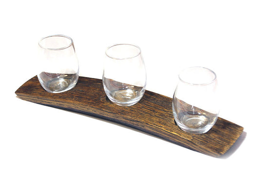 A handcrafted wooden wine flight with three small taster glasses, set on a curved piece of wood with a rich grain finish.