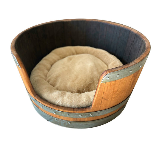 A pet bed made from a red wine barrel with a beige cushion inside.
