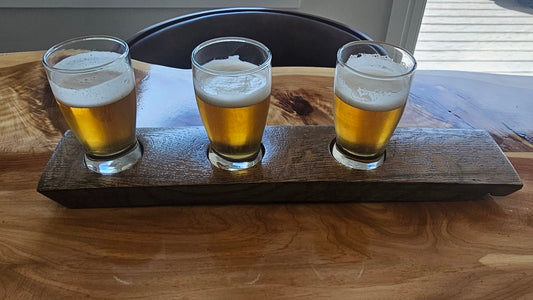 Three glasses of beer on a wooden tray with a blurred background