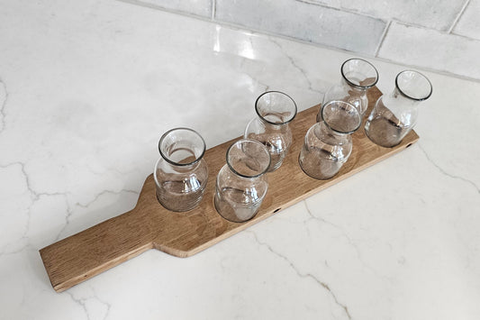 Wooden tray with six clear glass tumblers on a light marble floor.