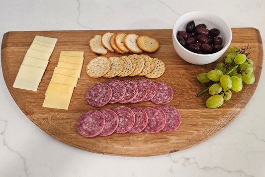 Wooden cutting board with sliced salami, cheese, crackers, and grapes on a marble surface.