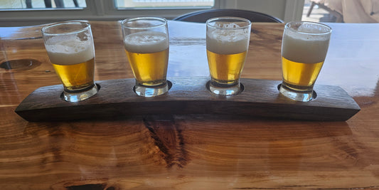 Four beer glasses with a wooden flight paddle on a wooden table.
