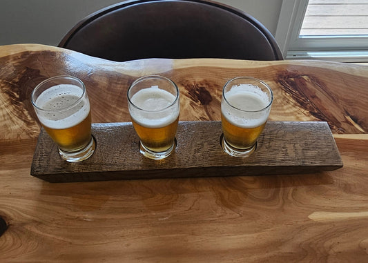 Three beer glasses on a wooden tray on a wooden surface.