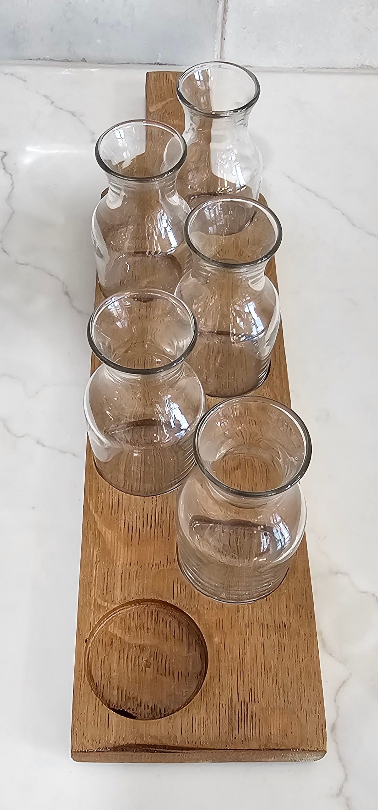 Wooden wall-mounted glass holder with six clear glasses on a marble wall.