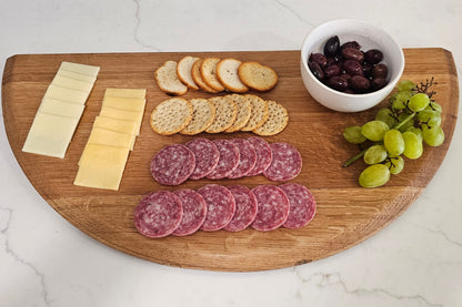 Wooden cutting board with sliced salami, cheese, crackers, and grapes on a marble surface.