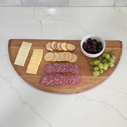 Wooden cutting board with sliced meats, cheese, and grapes on a kitchen counter.