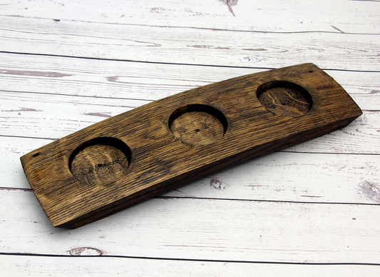 Dark walnut wine barrel stave dessert and dip flight server with three carved bowl holders angled on rustic white background