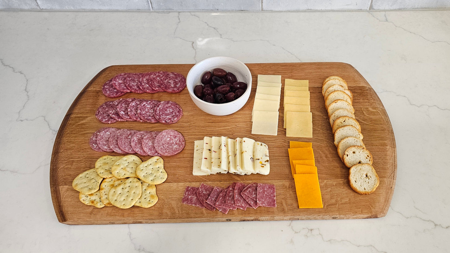 Wooden cutting board with various sliced meats, cheeses, and crackers on a kitchen counter.