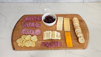 Wooden cutting board with various sliced meats, cheeses, and crackers on a kitchen counter.