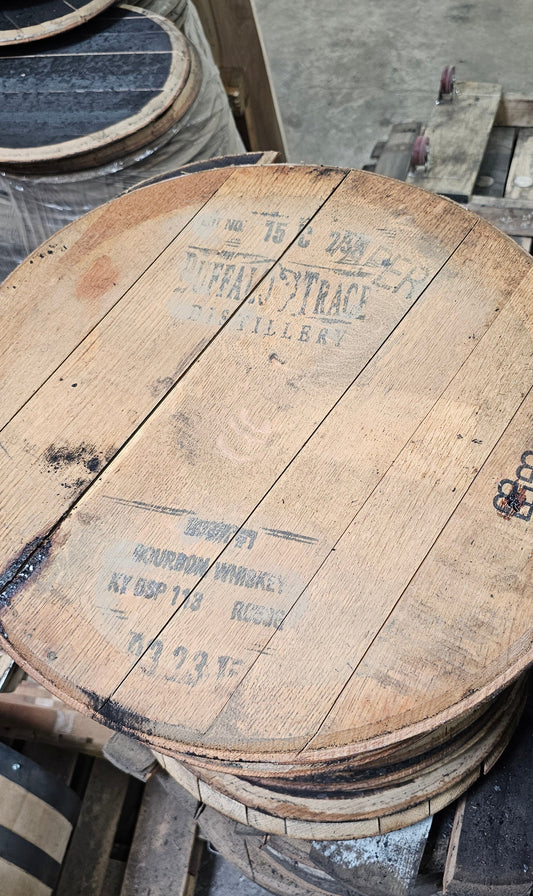 Stack of wooden whiskey barrel heads with visible branding on a concrete floor.