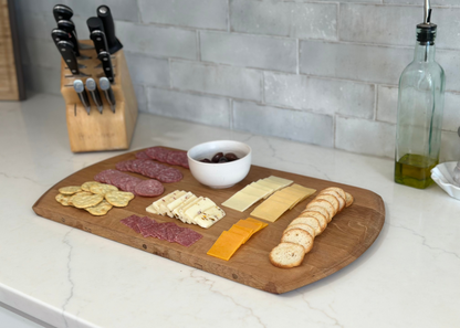 Wooden cutting board with sliced meats, cheeses, and bread on a kitchen counter.