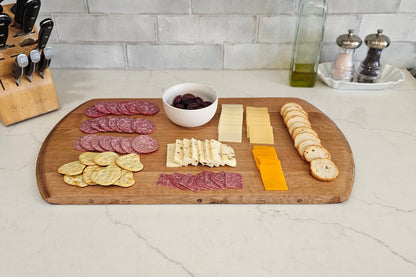 Wooden cutting board with sliced meats, cheeses, and olives on a kitchen counter.