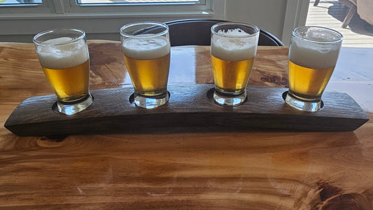 Four glasses of beer on a wooden paddle on a wooden table.