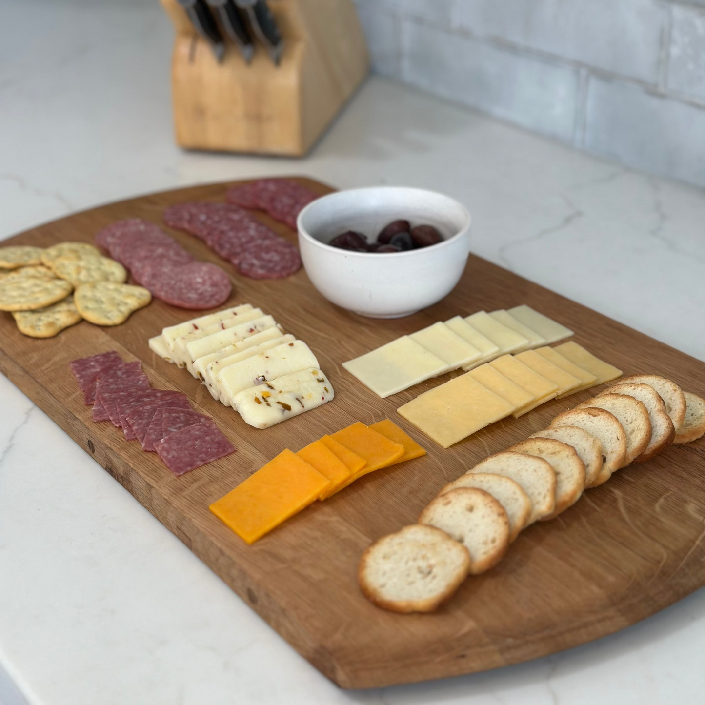 Wooden cutting board with assorted meats, cheeses, and crackers on a kitchen counter.