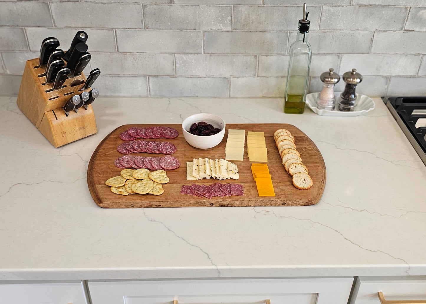 Kitchen counter with a cutting board displaying various types of cheese and meats, next to a knife block and stove.